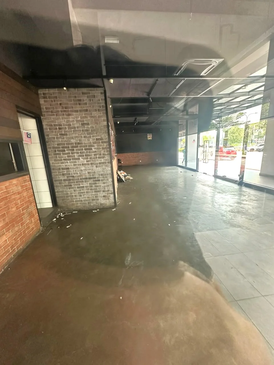 Room features: exposed brick wall, grey painted walls, polished concrete flooring, large glass windows, open layout, high ceiling, recessed lighting, visible trash on floor; style: modern; view: street.